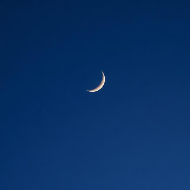 夜空中彎彎的弦月高掛，形狀宛如一把鋒利的鐮刀，月光灑落在寧靜的村莊屋頂上
